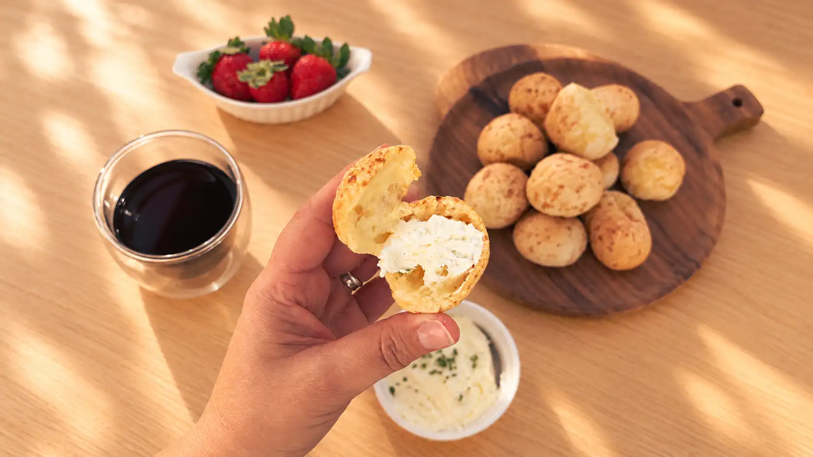 A hand holding opened cheese bread with cream cheese beside a bowl of cream cheese
